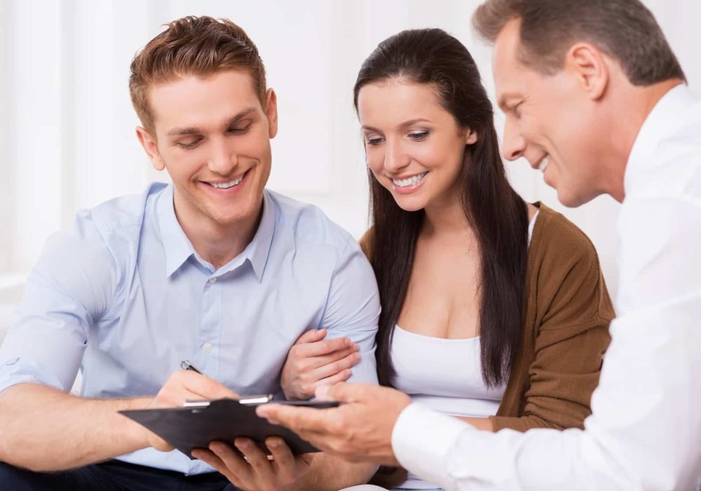 Just sign here. Happy young couple signing documents while confident mature man holding clipboard and smiling